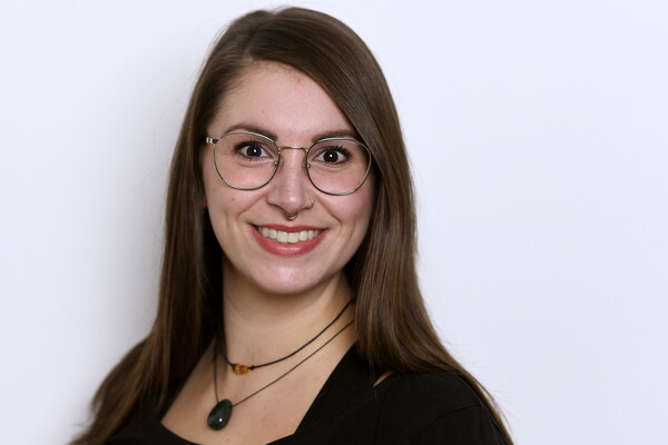 Porträt von Nathalie Benne. Sie trägt eine Brille, hat langes braunes Haar und lächelt in die Kamera. Im Hintergrund eine helle, neutrale Wand.