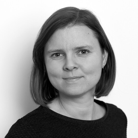 Porträt von Carolin Heckel. Sie hat kinnlanges, glattes, braunes Haar und trägt ein dunkles Oberteil. Sie blickt ruhig und freundlich in die Kamera, vor einem hellen Hintergrund.